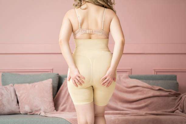 Woman in beige full-coverage shapewear shorts from behind, hands on her buttocks.