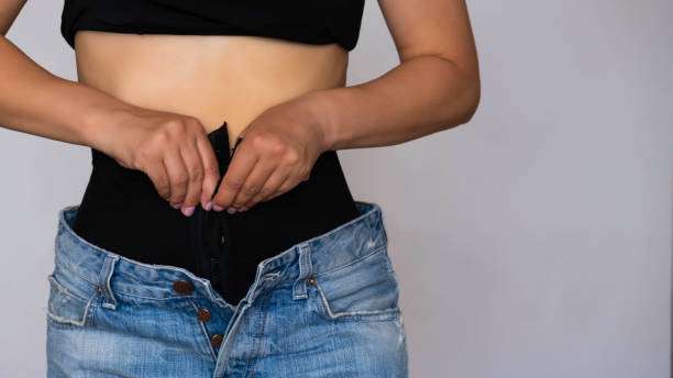 Woman fastening black shapewear under jeans, achieving a smooth silhouette.